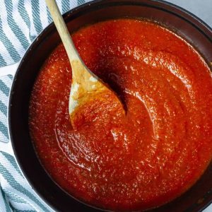 Homemade marinara sauce being stirred with a wooden spoon in a large Dutch oven.