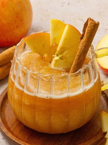 apple cider slushie in a glass mug garnished with apples and cinnamon stick