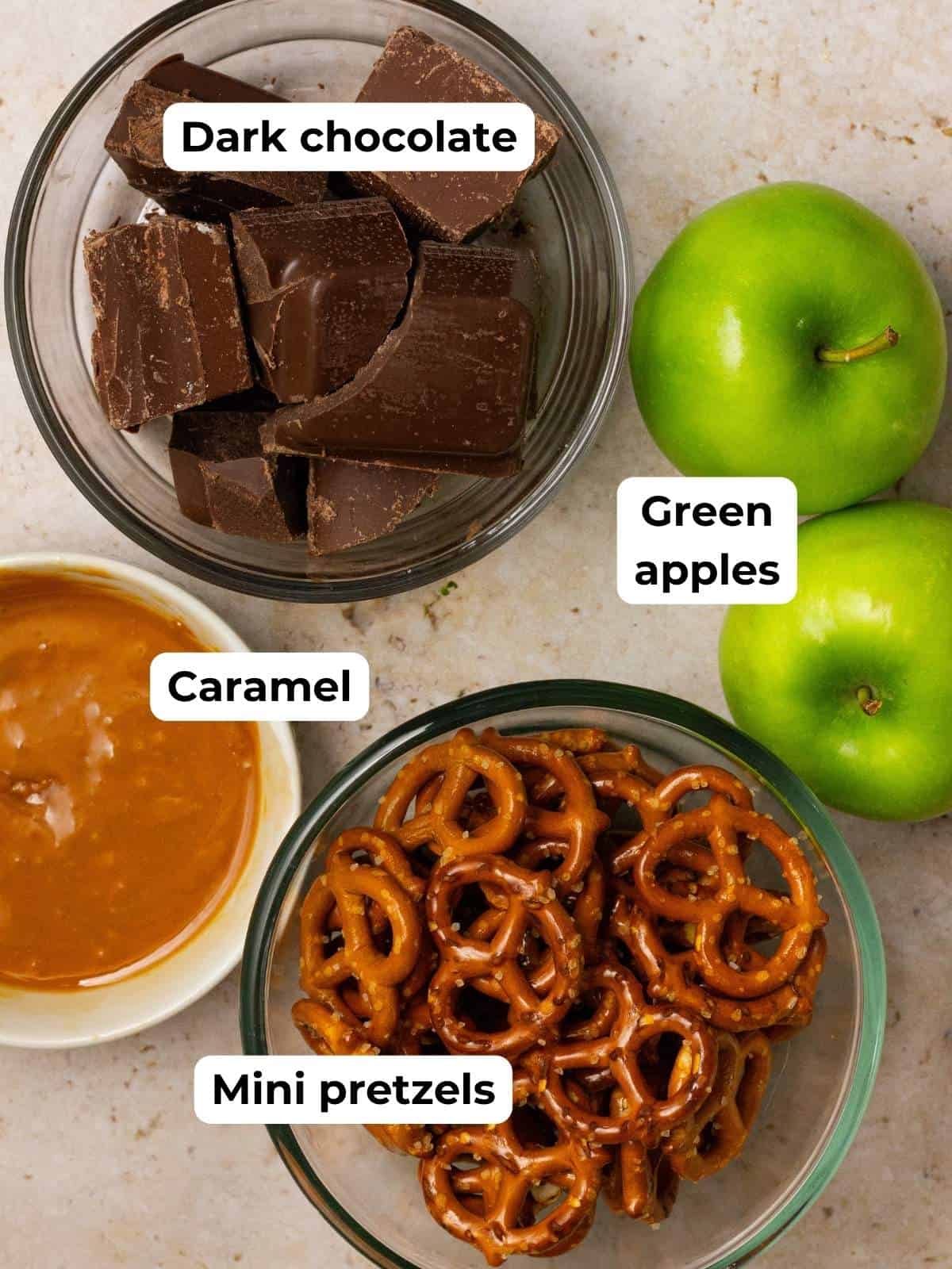 Ingredients to make caramel apple chocolate bark with pretzels on a tan counter.