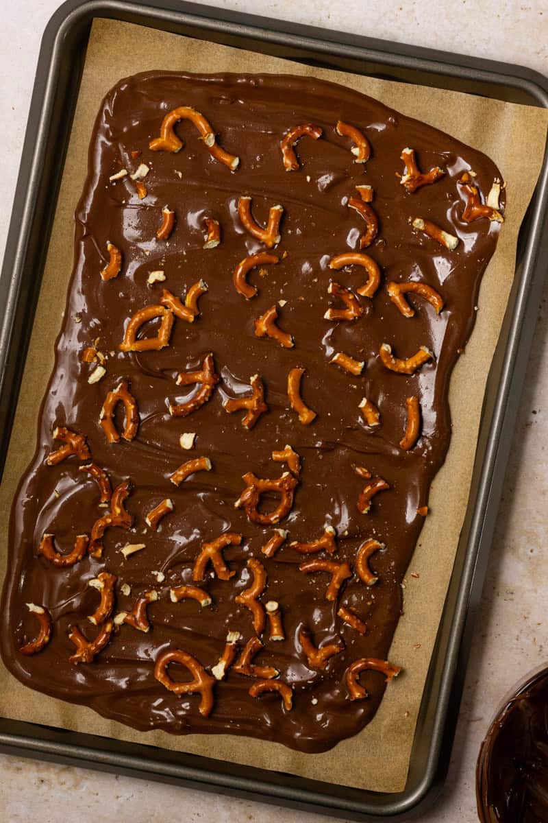 Melted chocolate spread on a pan with pretzel pieces scattered throughout.