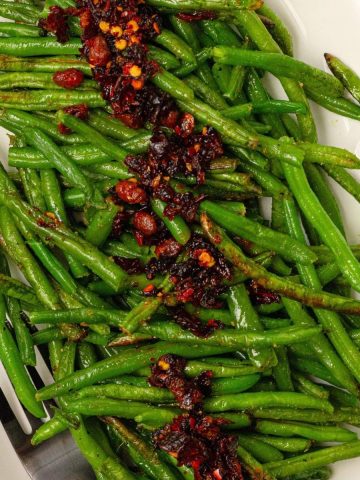 roasted green beans with chili crunch on a white plate