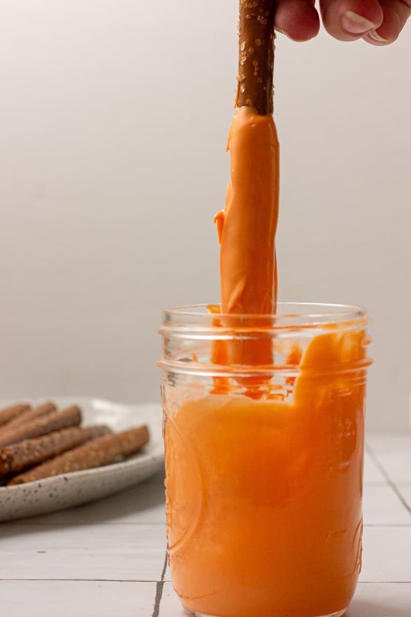 pretzel rod being dipped in orange chocolate 