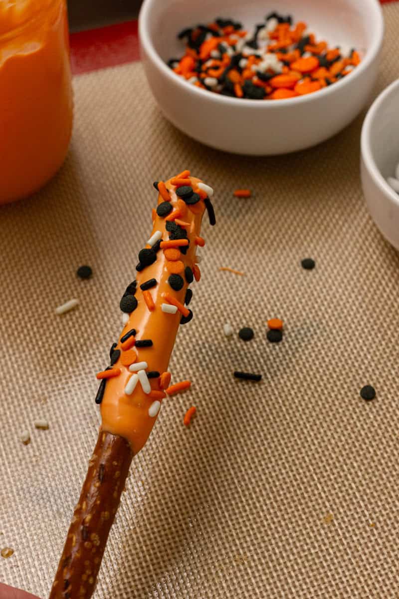 orange chocolate covered pretzel rod with halloween themed sprinkles 