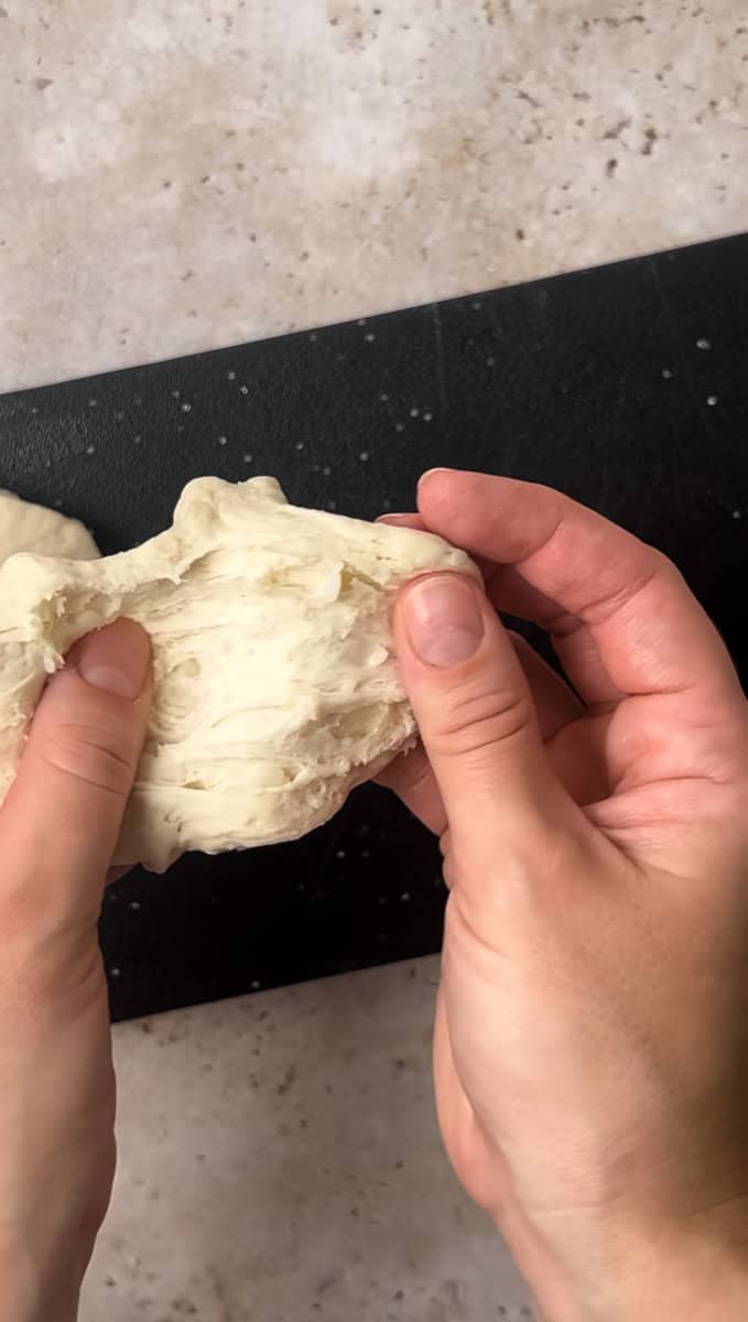 Hands splitting dough on a black cutting board.
