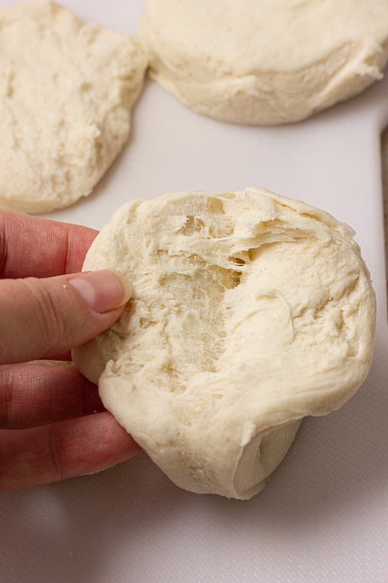 A hand holding a piece of uncooked biscuit dough.