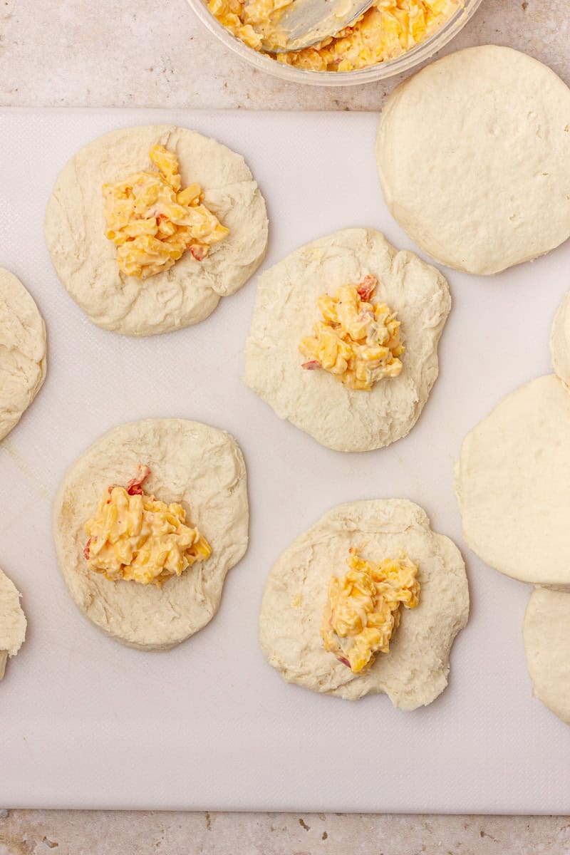 Dough circles on a cutting board are topped with pimento cheese.