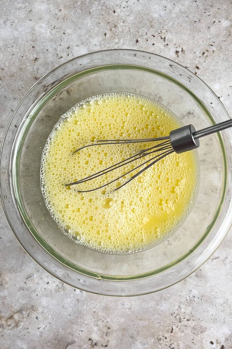 Eggs and broth being whisked together in a glass bowl, ready for the stuffing.