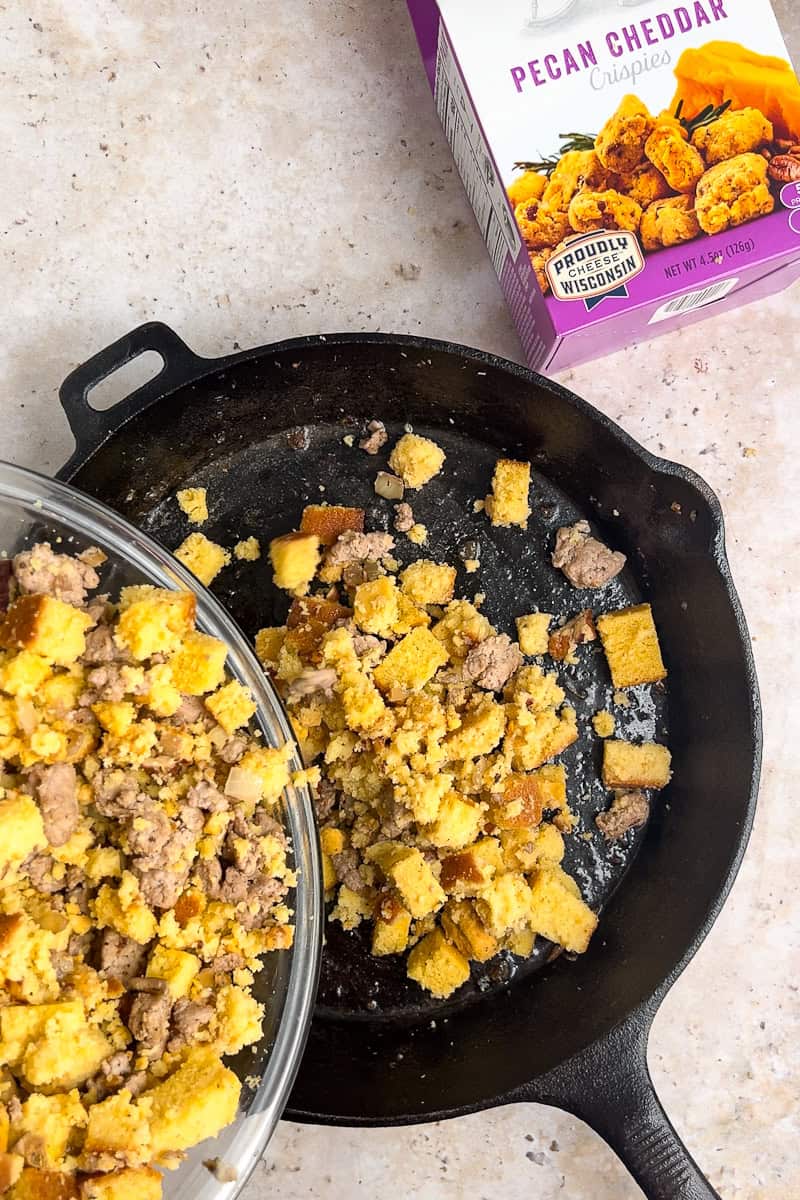 Stuffing mixture being poured into a cast iron skillet for baking.