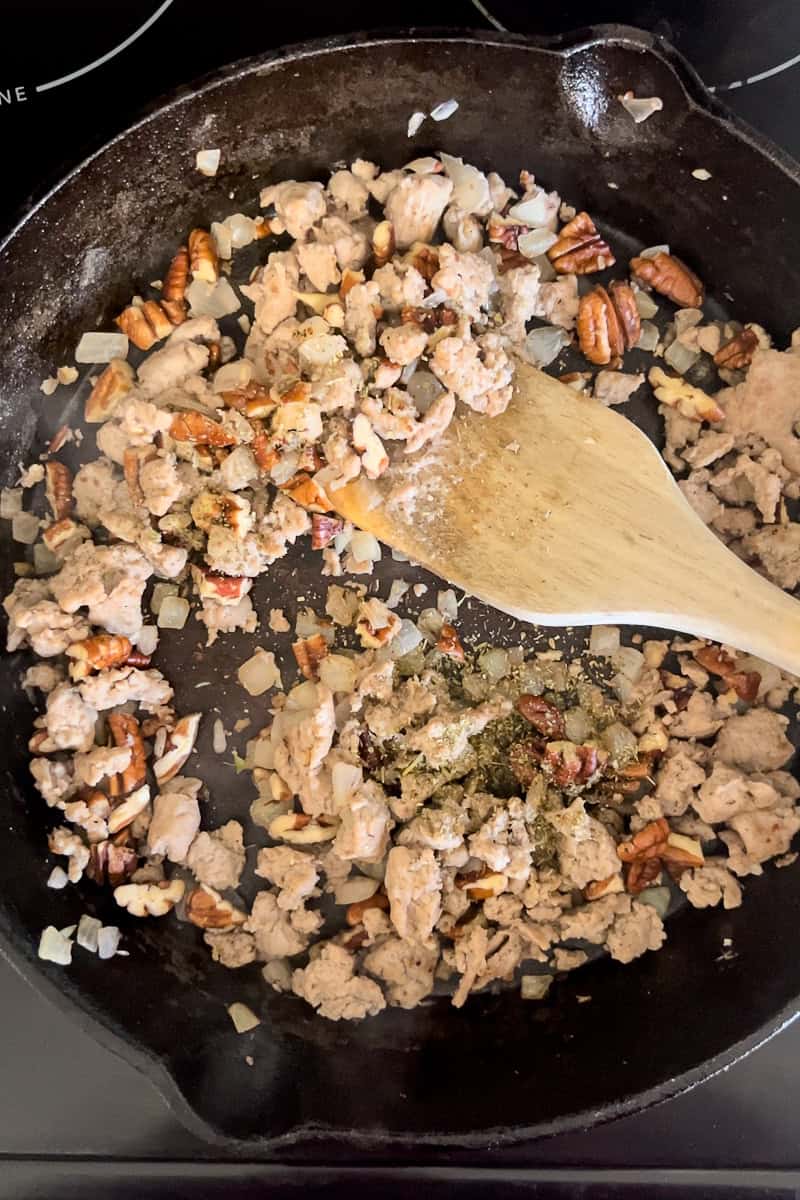 Ground turkey, pecans, and fresh herbs sautéing in a cast iron skillet.