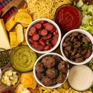 An epic pasta charcuterie board with spaghetti, penne, beef meatballs, sausage, steak tips, sauces, salad, and garlic bread.