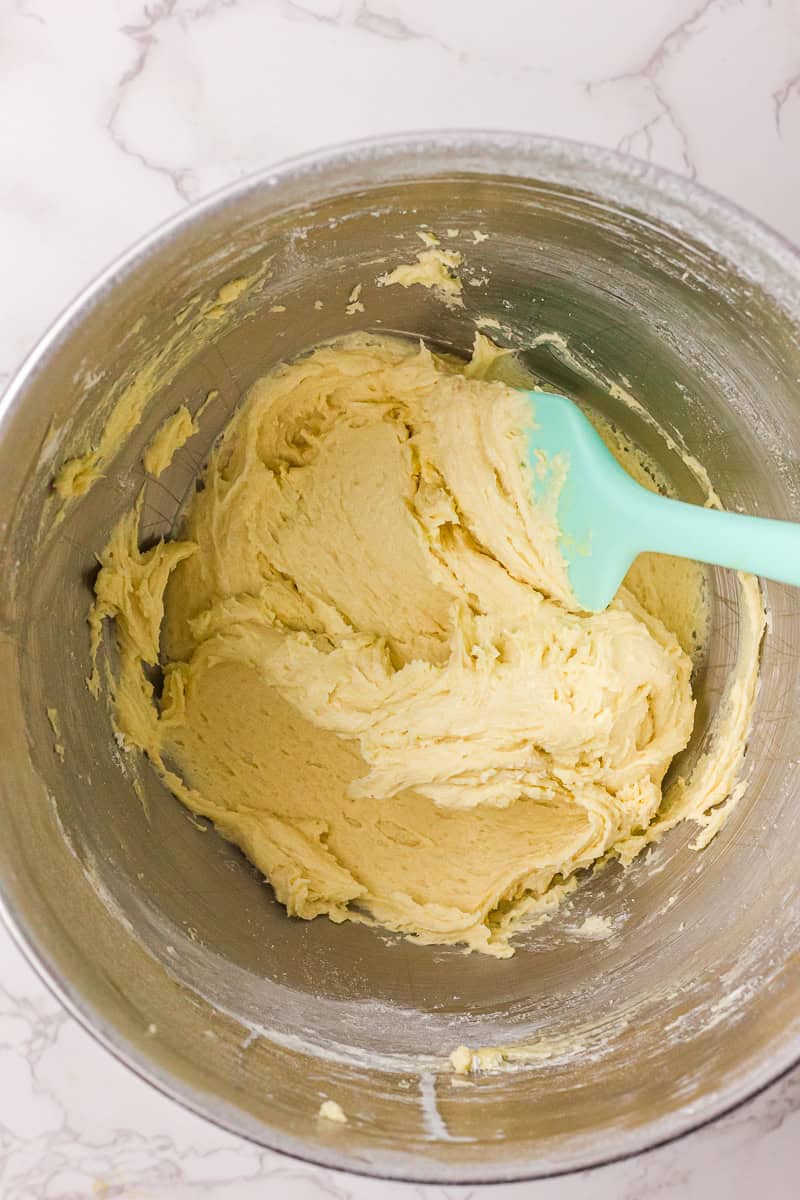 Sugar cookie dough is mixed in a metal bowl with a spatula resting inside.