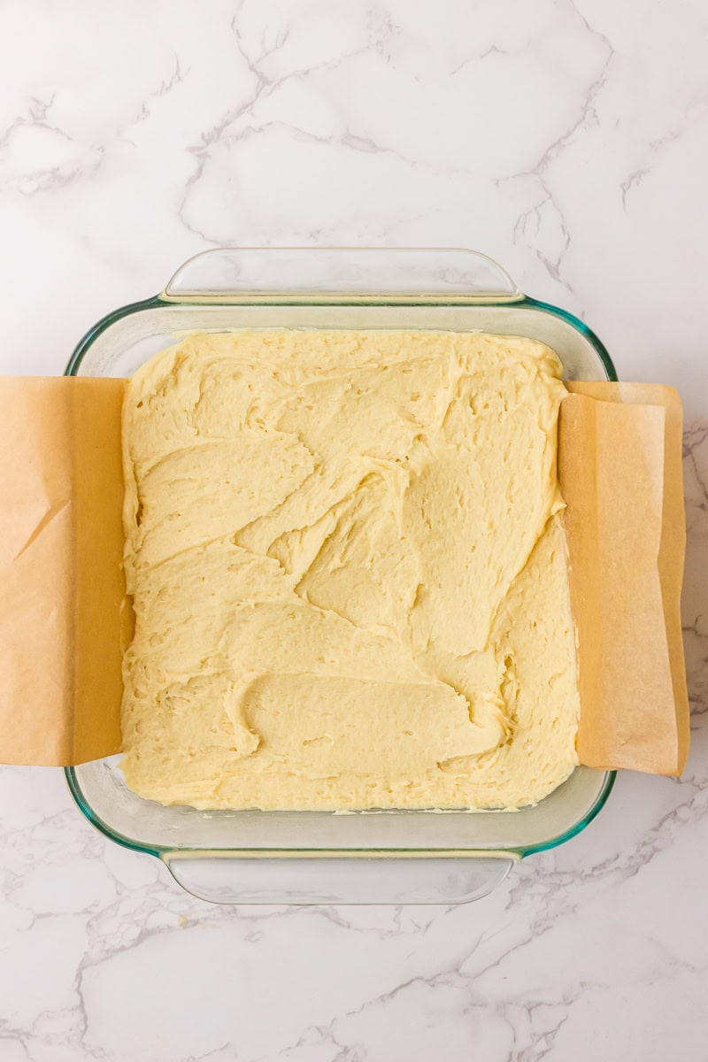The sugar cookie dough is spread evenly into a parchment-lined glass baking dish before baking.
