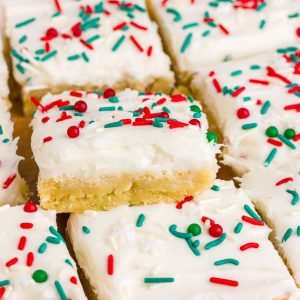 Frosted Christmas sugar cookie bars are stacked and topped with red, green, and white sprinkles.