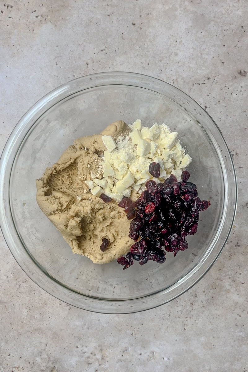 A bowl of cookie dough with white chocolate chunks and dried cranberries ready to be mixed in.