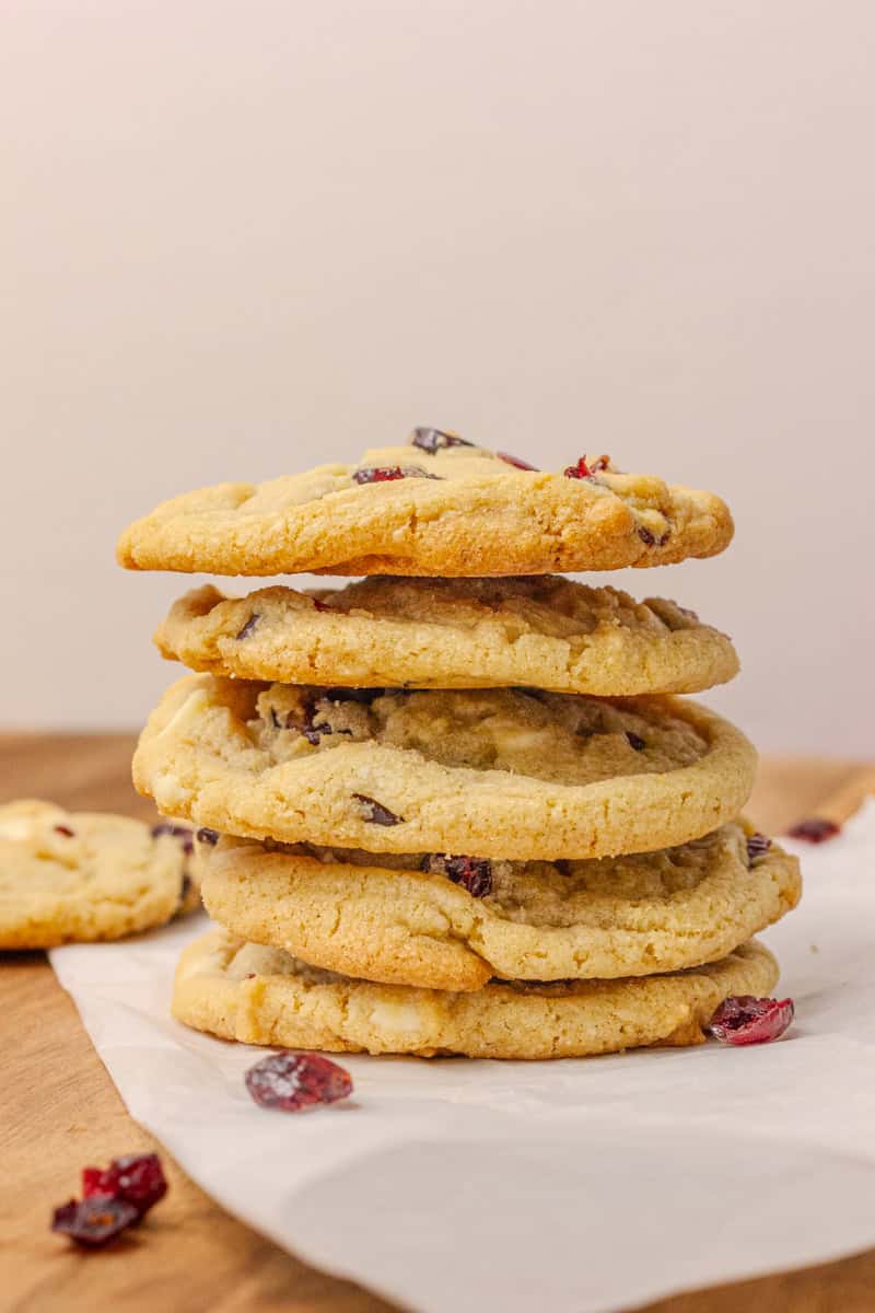 A stack of Cranberry Orange White Chocolate Cookies on a wooden surface, garnished with dried cranberries.