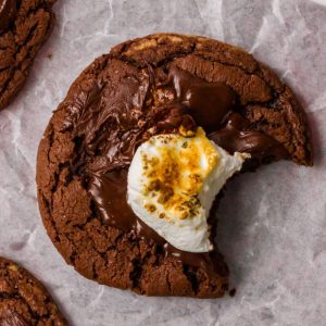 A close-up of a hot chocolate cookie topped with melted chocolate and a toasted marshmallow.