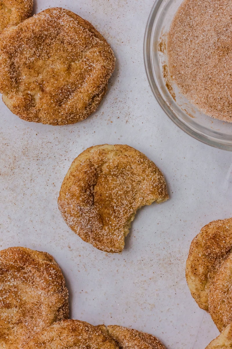 A snickerdoodle cookie with a bite taken out, laying on parchment paper.

