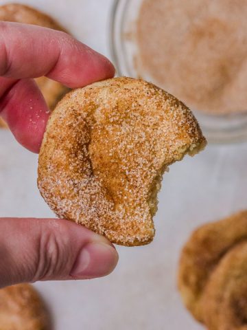 A mini snickerdoodle cookie with a bite taken out, held in a hand.