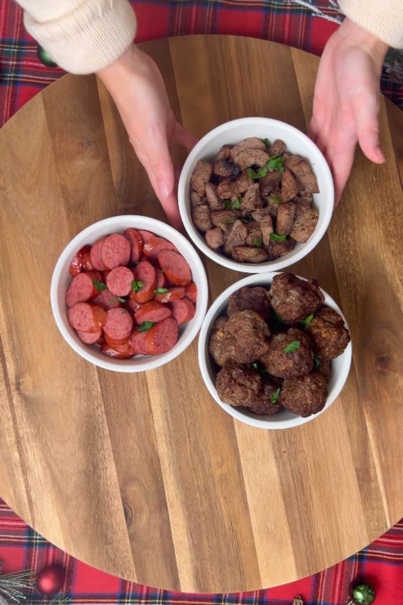 Placing bowls of beef meatballs, steak tips, and sausage in the center of the wooden board.