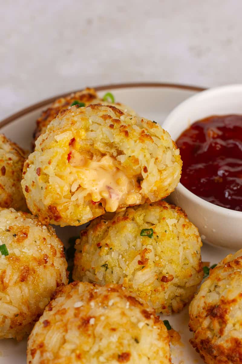 Crispy pimento cheese rice ball broken open, showing a gooey cheese center with red pepper jelly on the side.