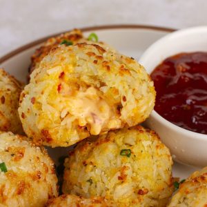 Crispy pimento cheese rice ball broken open, showing a gooey cheese center with red pepper jelly on the side.