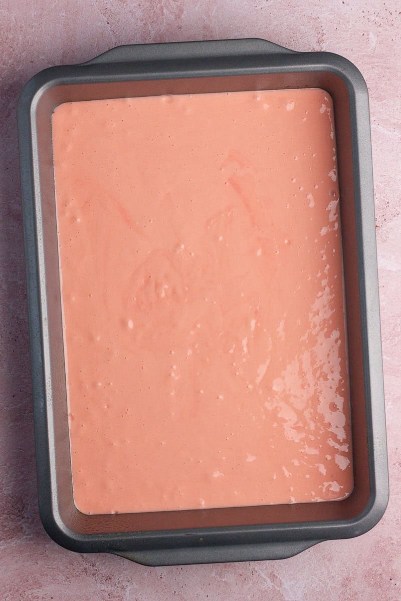 A baking pan filled with smooth, pink strawberry cake batter, ready to be baked.