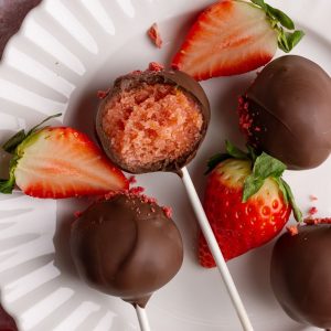 Chocolate strawberry cake pops on white plate with a bite taken out.