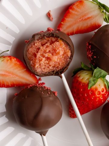 Chocolate strawberry cake pops on white plate with a bite taken out.