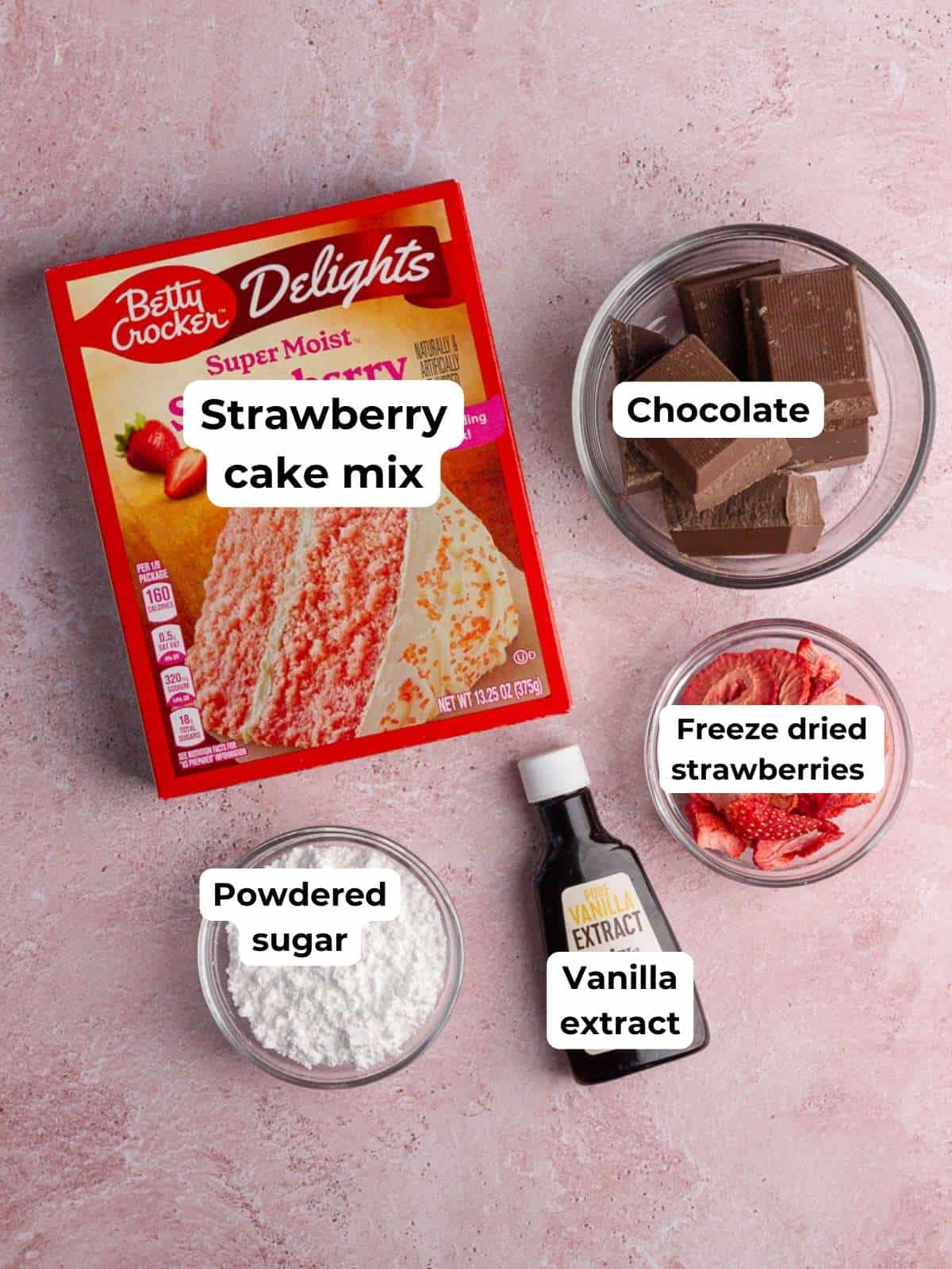 Ingredients for chocolate-covered strawberry cake pops, including strawberry cake mix, chocolate, powdered sugar, vanilla extract, and freeze-dried strawberries.