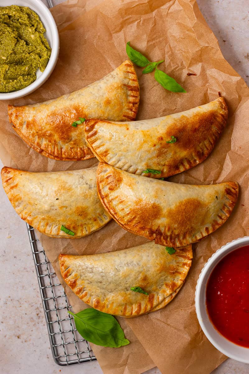 Golden-brown air-fried empanadas caprese on parchment paper, served with pesto and marinara sauce.
