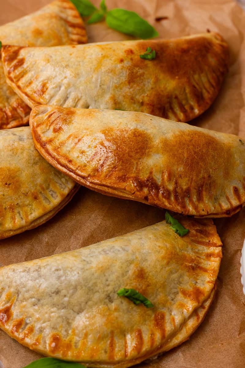 A plated batch of golden-brown empanadas caprese garnished with fresh basil, ready to serve.