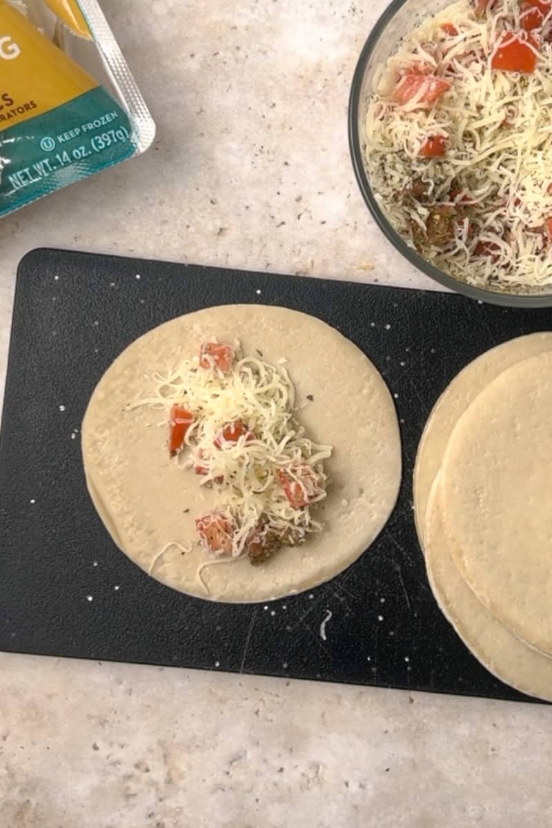 An empanada disc with a portion of mozzarella, tomato, and seasoning filling placed in the center.