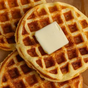 A close-up of crispy Jiffy cornbread waffles with butter melting on top.