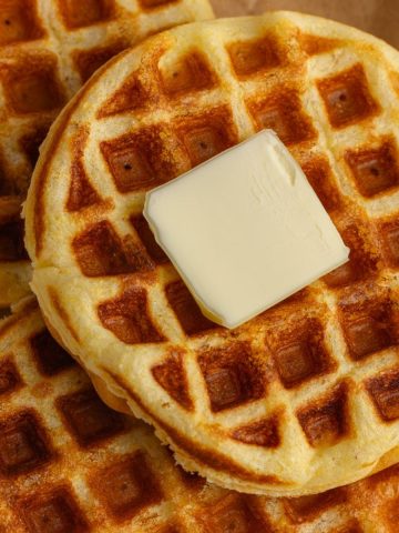 A close-up of crispy Jiffy cornbread waffles with butter melting on top.