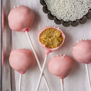 A close-up of pink cake pops with a smooth chocolate coating and white sprinkles, showcasing the final product.
