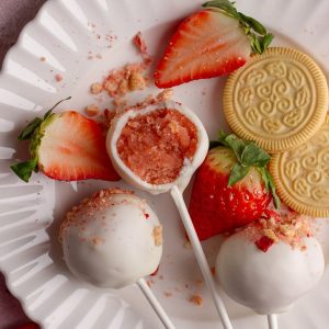 Strawberry cake pops on white plate with bite taken out.