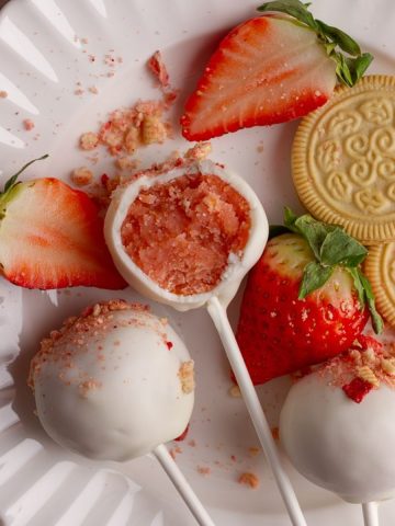 Strawberry cake pops on white plate with bite taken out.