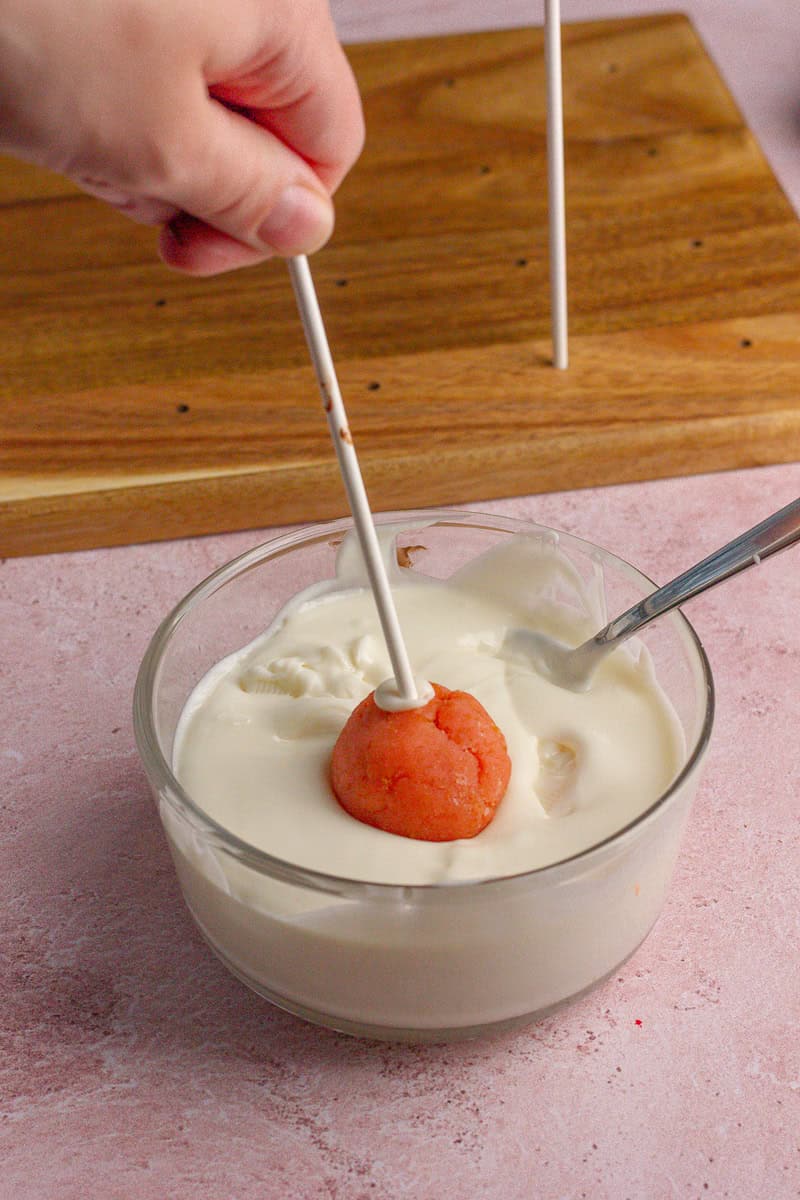 A cake pop being dipped into melted white chocolate coating.