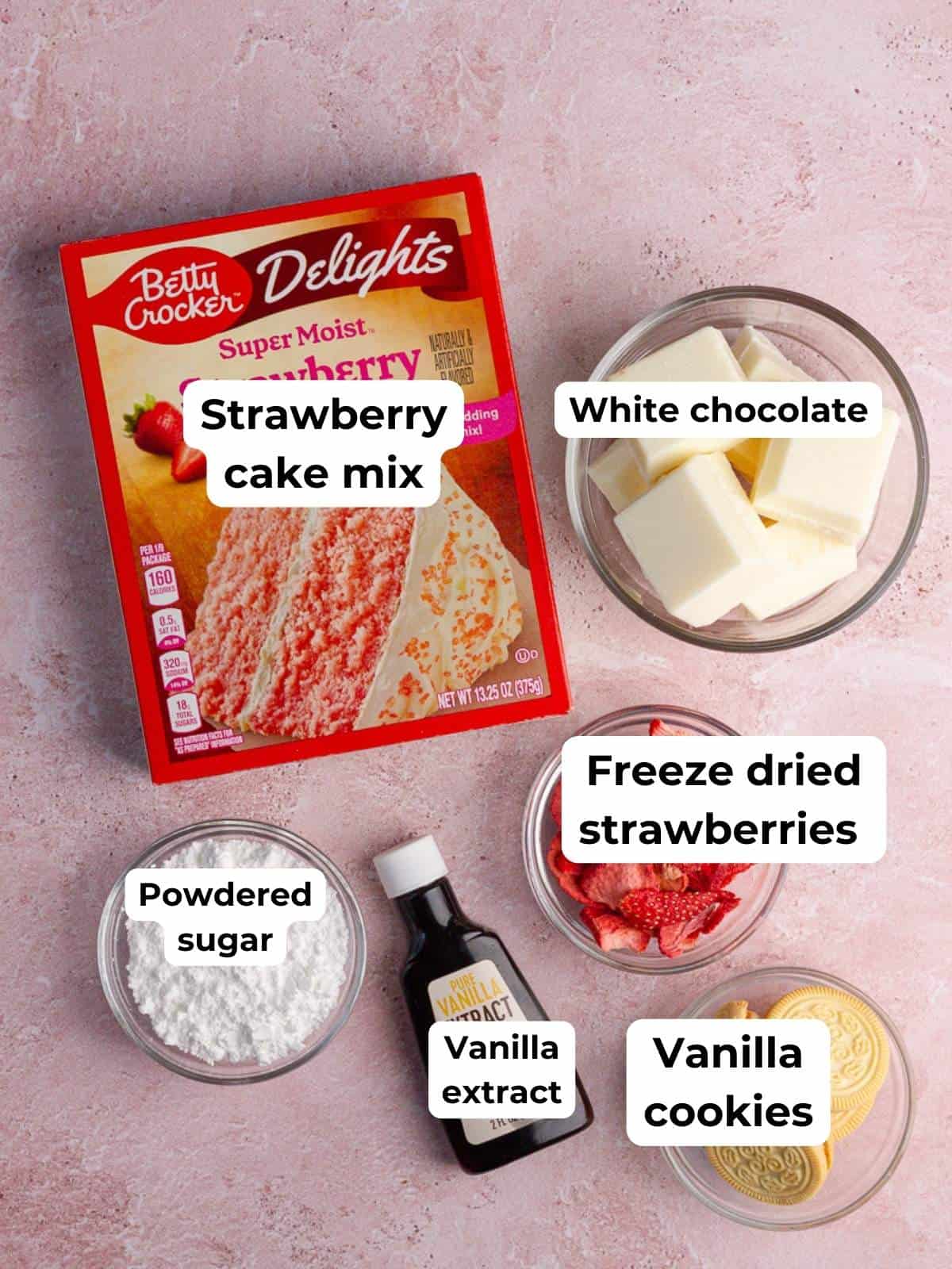 Ingredients for strawberry cake pops, including cake mix, white chocolate, vanilla extract, powdered sugar, freeze-dried strawberries, and golden sandwich cookies.