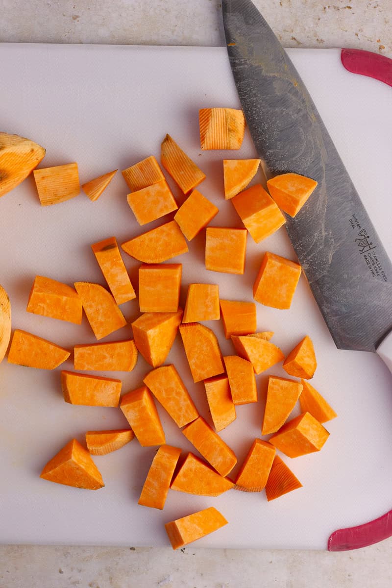 Chopped sweet potatoes on a cutting board with a knife.