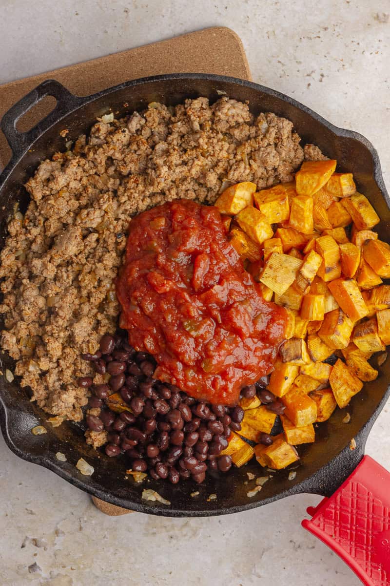 Cooked ground turkey, roasted sweet potatoes, black beans, and salsa in a skillet.