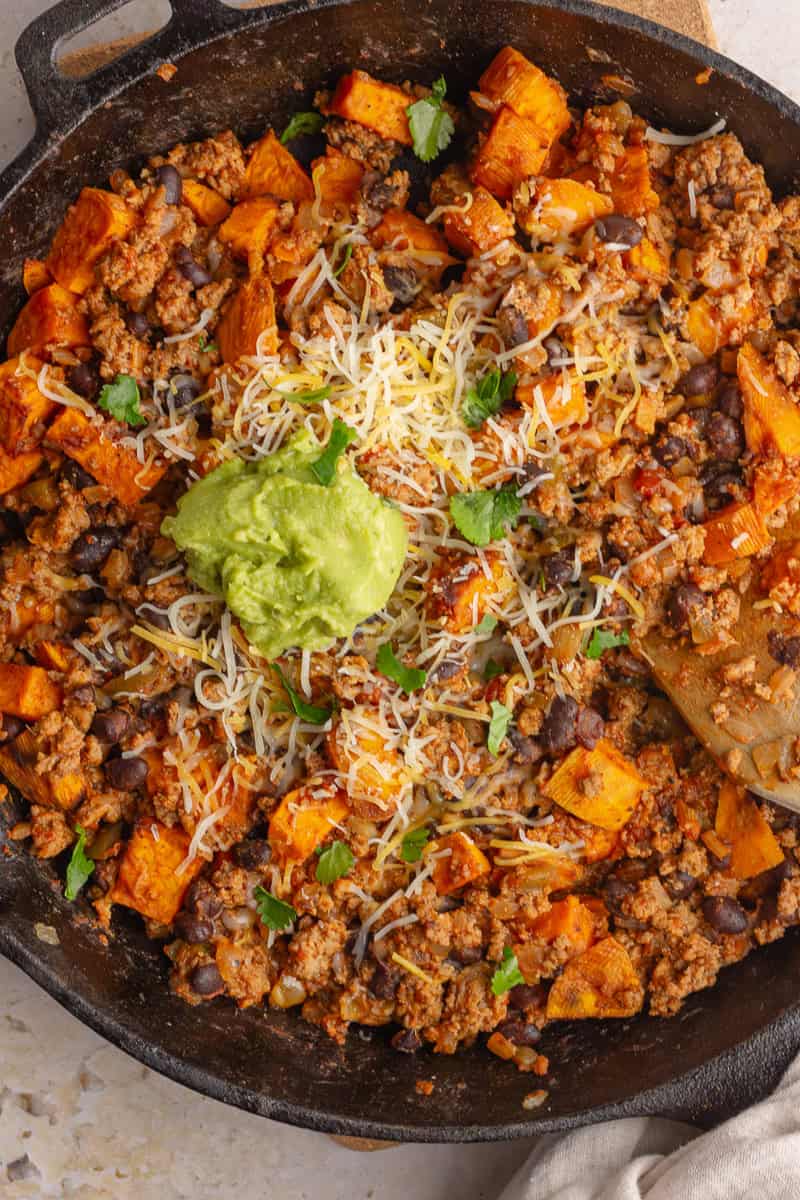 Sweet potato taco skillet topped with shredded cheese and avocado.