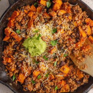 Close-up of sweet potato taco skillet with melted cheese and avocado.