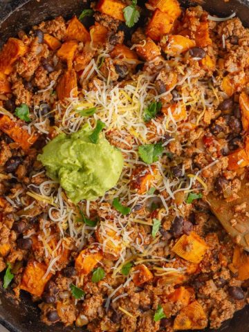 Close-up of sweet potato taco skillet with melted cheese and avocado.