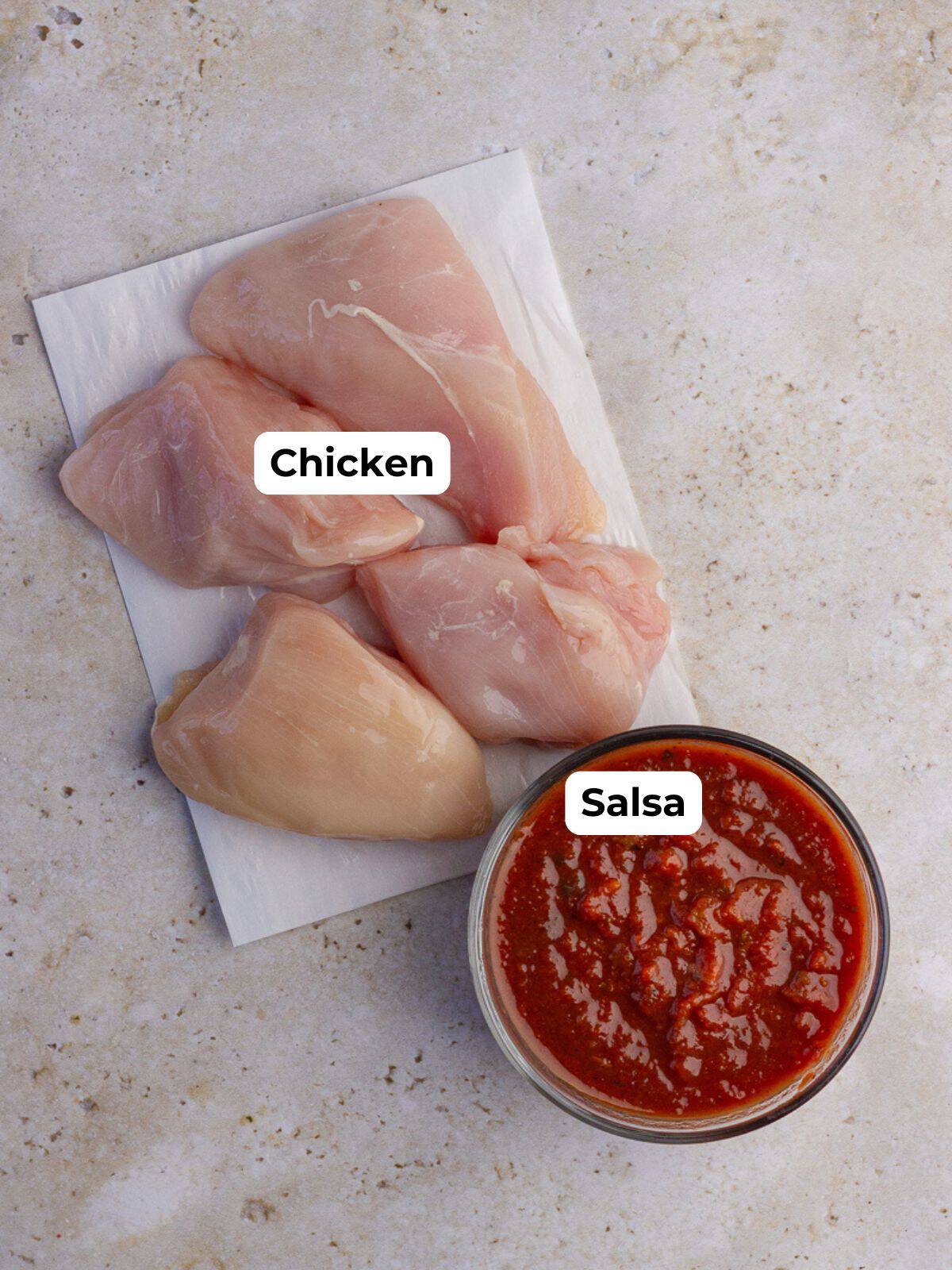 Raw chicken breasts and a bowl of salsa labeled as ingredients for crock pot enchilada chicken.