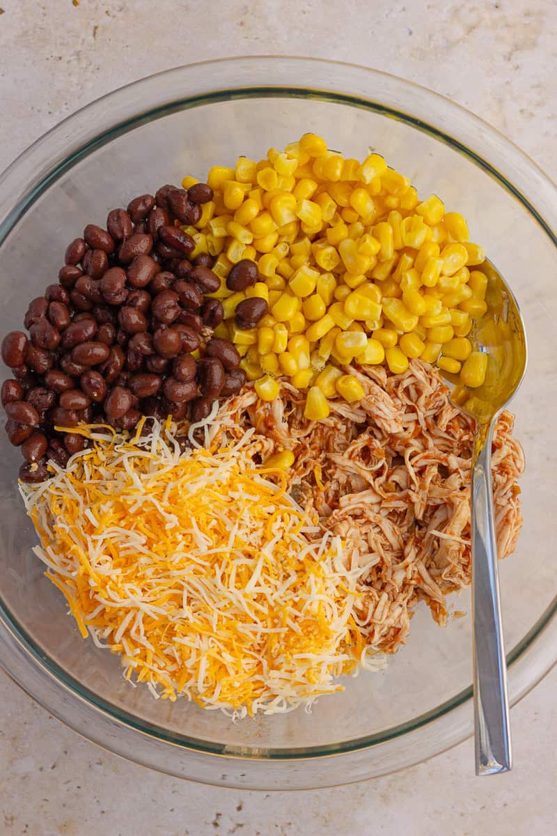 A bowl filled with shredded chicken, black beans, corn, and shredded cheese.