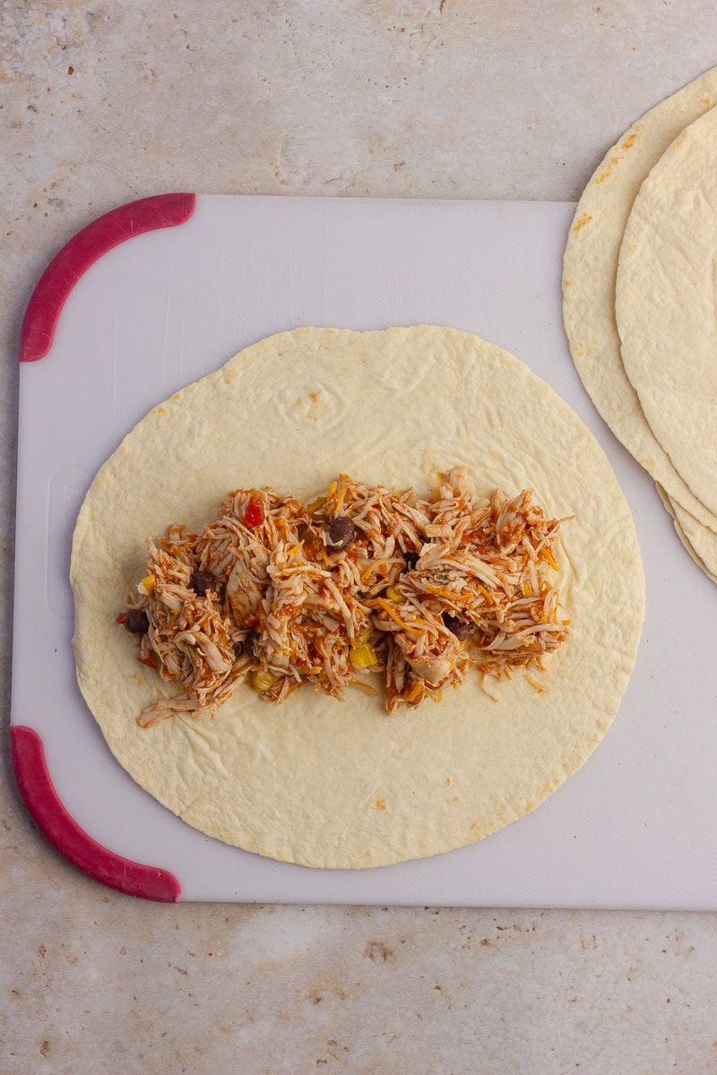A flour tortilla on a cutting board with enchilada filling spread in the center.