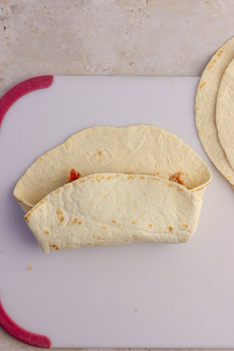 A flour tortilla being folded over the enchilada filling.