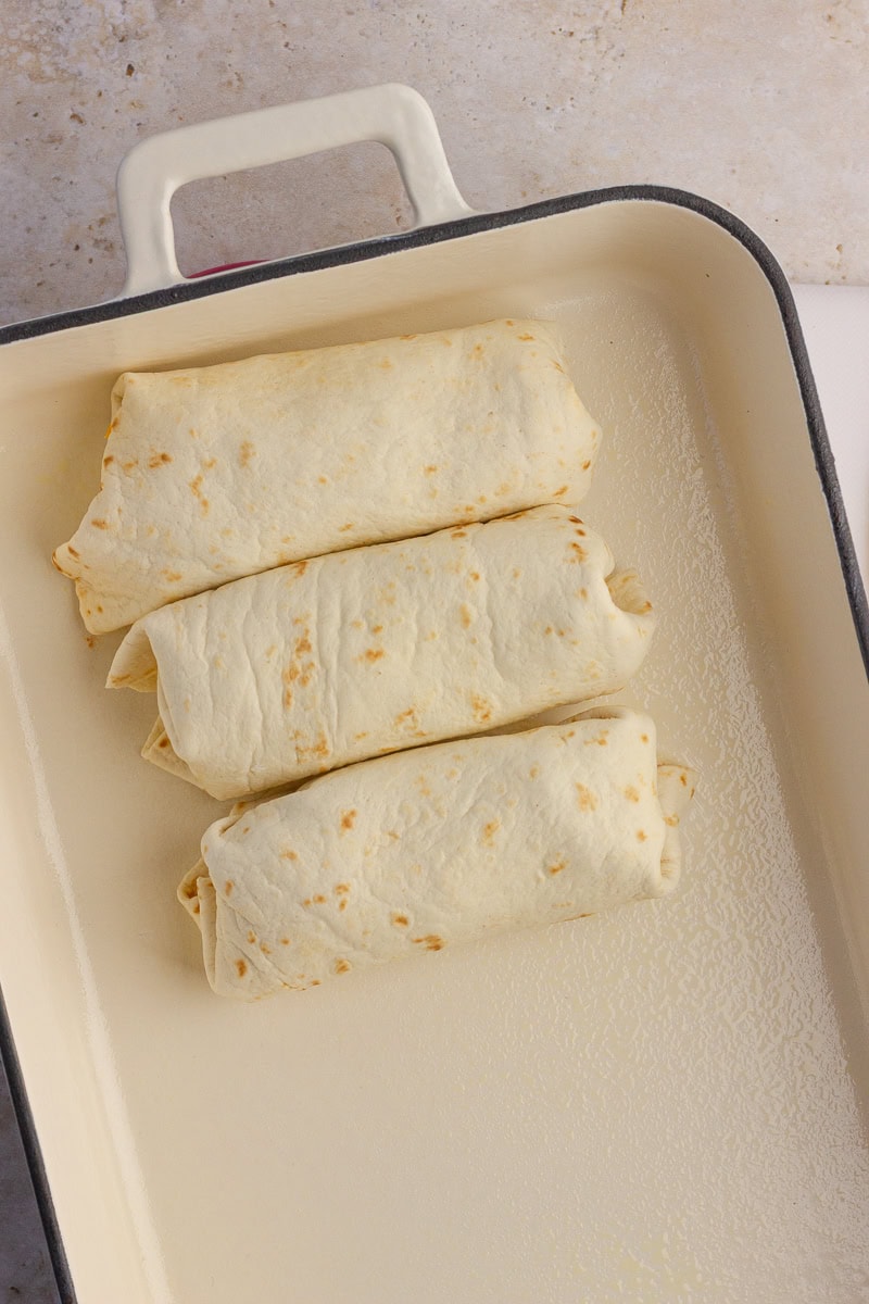 Three rolled enchiladas placed seam-side down in a baking dish.