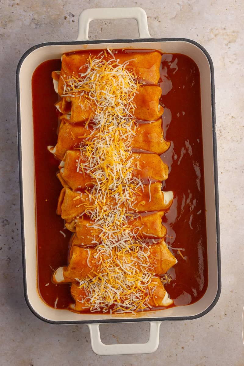 Rolled enchiladas covered in red enchilada sauce and topped with shredded cheese.